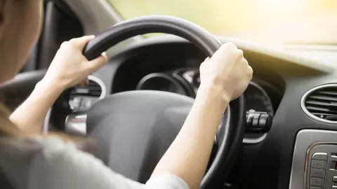 Close up of female hands on the steering. Traveler girl on car trip, looking at the road. View over shoulder