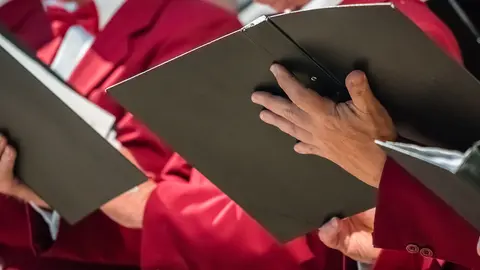 Close up of mens choir members holding singing book while performing in a cathedral in Rochester, Kent, UK