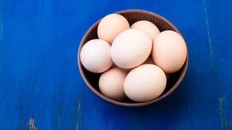 Fresh eggs in a brown bowl on  blue background. Top view.