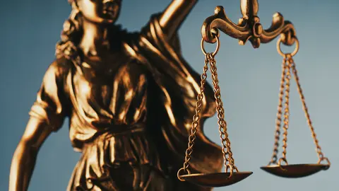 Figure of Justitia or Justice holding the scales of justice with close up focus to the scales symbolic of the law over grey