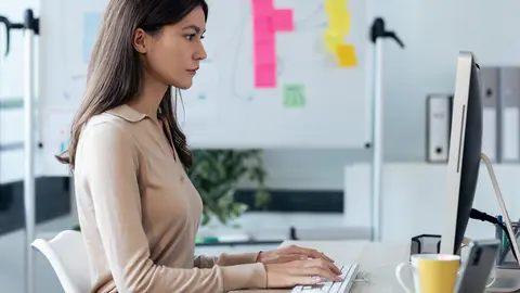 Shot of beautiful young business woman working with computer while sitting in desk in modern startup office.